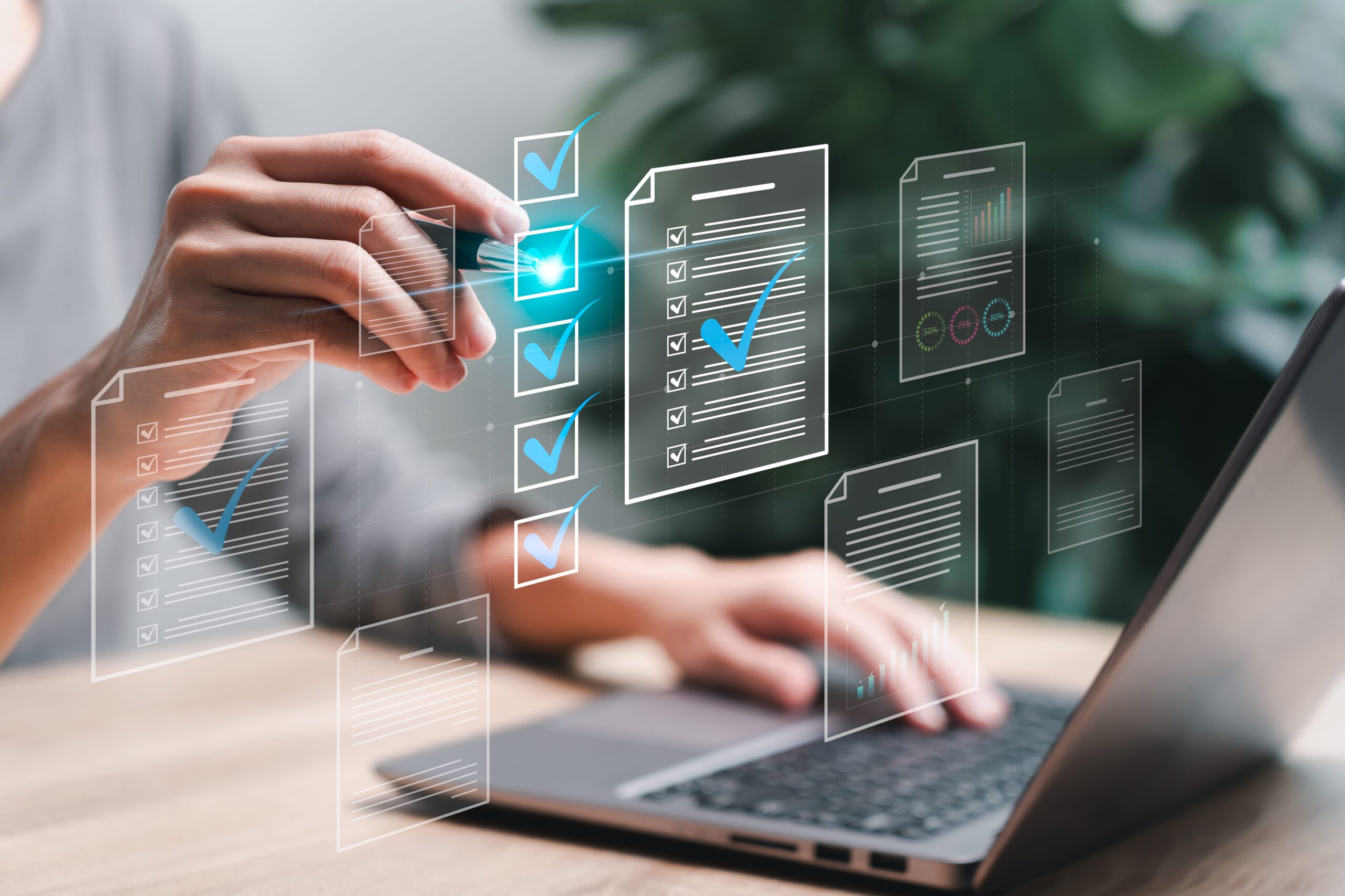 Eine Hand markiert Dokumente mit Häkchen, während ein Laptop im Hintergrund sichtbar ist.